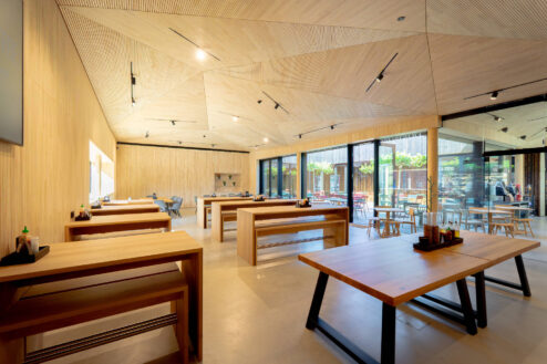 Großer, heller Gastraum mit Holzdecken und -wänden sowie großzügigen Sitzgelegenheiten und Blick auf eine begrünte Außenterrasse.