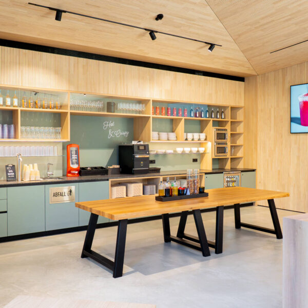 Selbstbedienungsbereich mit Getränkespendern, Kaffeemaschine und Gläsern, aufgeräumt und funktional gestaltet im natürlichen Holzdesign.