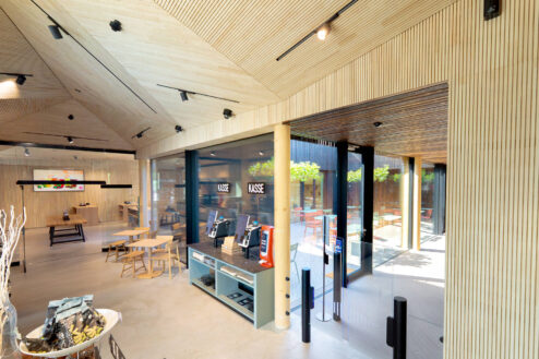 Kassenbereich mit modernen Self-Service-Terminals, gläserner Eingangstür und Blick auf die Außenterrasse eines stylischen Lokals.