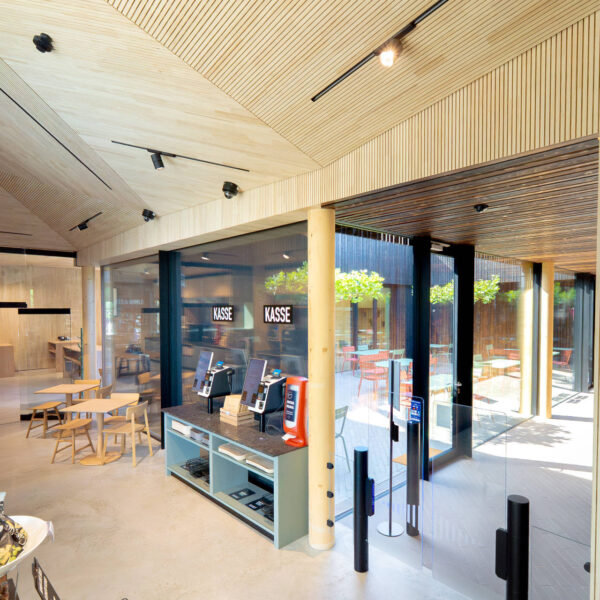 Kassenbereich mit modernen Self-Service-Terminals, gläserner Eingangstür und Blick auf die Außenterrasse eines stylischen Lokals.