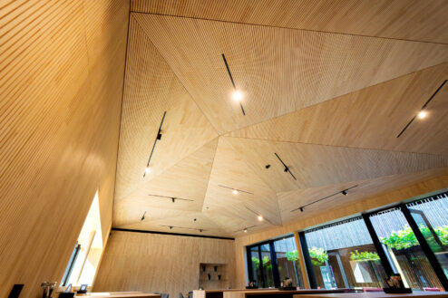 Detailaufnahme der geometrischen Holzdecke eines modernen Gastraums mit eleganter Lichtführung.