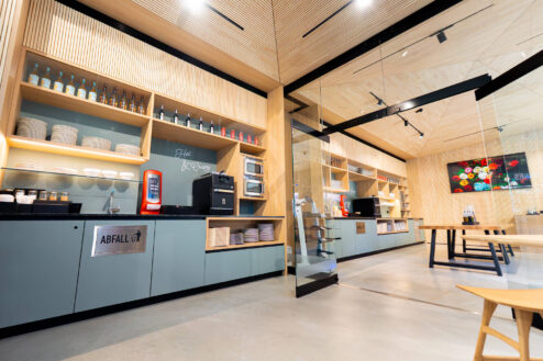 Langer Thekenbereich mit offener Regalanlage, integriertem Spülbereich, Kaffeemaschine und Stauraum – in klarem, minimalistischen Design.