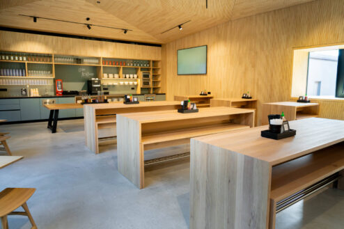 Offener Gastronomiebereich mit minimalistischen Holztischen und gut organisiertem Selbstbedienungstresen im Hintergrund.