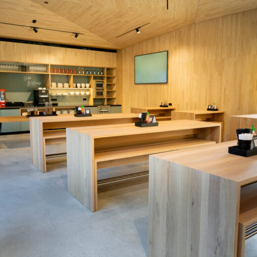 Offener Gastronomiebereich mit minimalistischen Holztischen und gut organisiertem Selbstbedienungstresen im Hintergrund.