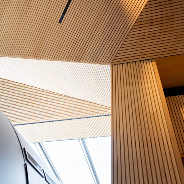 Architektonisches Detailbild der Decke mit schräg verlaufenden Holzlamellen und natürlichem Lichteinfall durch ein Oberlicht.
