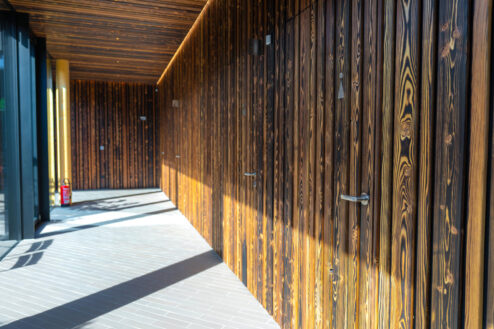 Überdachter Außenbereich mit dunkler Holzfassade und mehreren diskreten Zugangstüren.