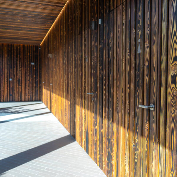 Überdachter Außenbereich mit dunkler Holzfassade und mehreren diskreten Zugangstüren.