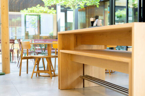 Detailaufnahme eines Hochtischs im Innenbereich mit Blick auf bunte Außenmöbel und grüne Bäume auf der Terrasse.