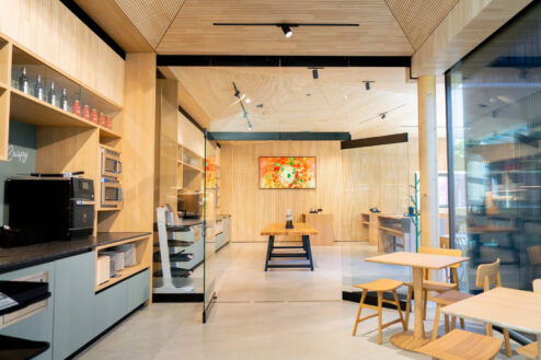 Einblick in den modernen Selbstbedienungsbereich mit Küchenzeile, Glastür und stilvollem Kunstwerk im angrenzenden Gastraum.