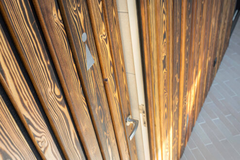 Nahaufnahme einer Toilettentür mit Piktogramm auf strukturierter, geflammter Holzfassade im Außenbereich.