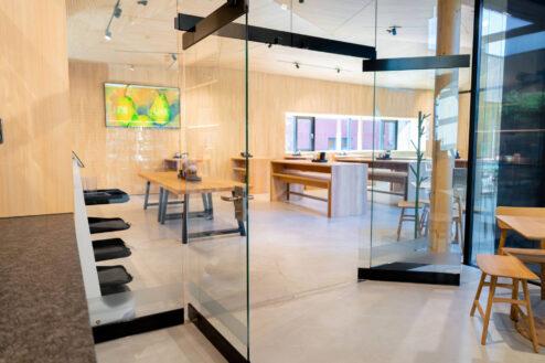 Geöffnete Glastür gibt den Blick frei auf einen lichtdurchfluteten Innenraum mit Sitzgelegenheiten aus hellem Holz.