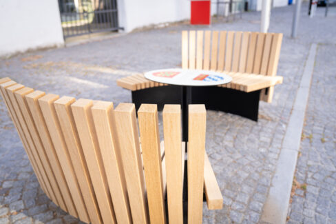Zwei halbrunde Sitzbänke aus Holz mit Tisch in der Mitte, fotografiert aus der Vogelperspektive.